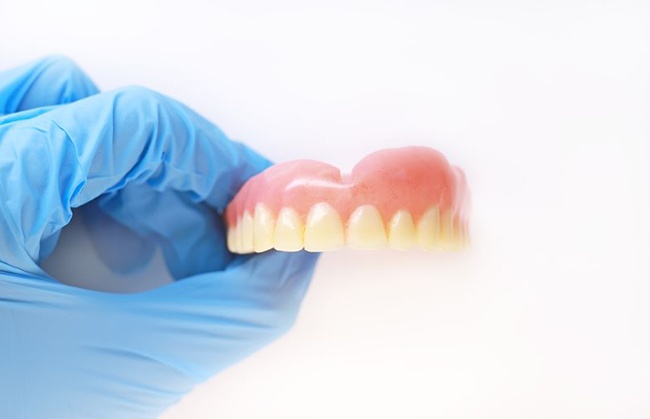 Gloved hand holding upper denture against white background