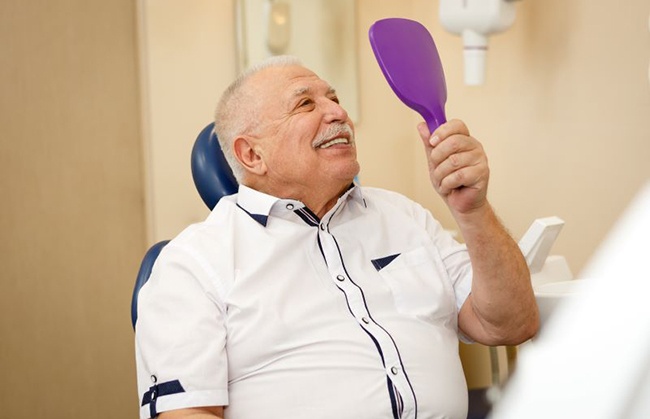 Senior dental patient holding mirror, admiring his dentures