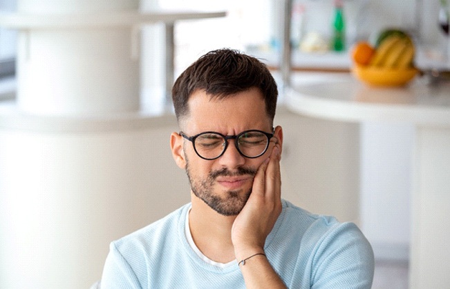 Man with glasses rubbing jaw due to tooth pain