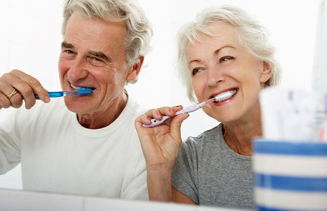 older couple brushing teeth in bathroom 