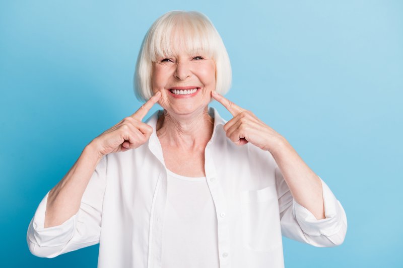 An older woman smiling and pointing at her bright white dentures